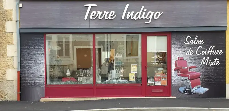 La façade du salon : enseigne Terre Indigo, mur de briques grises, vitrine au cadre rouge et fauteuil de barbier peint