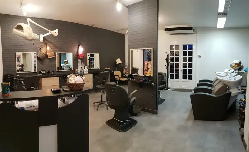 L'intérieur du salon : comptoir d'accueil, postes face aux miroirs sur un mur de briques grises, fauteuil de barbier et bacs de lavage